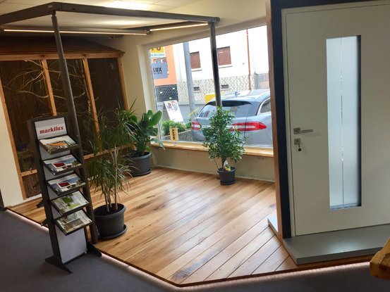 Moderner Ausstellungsraum mit Holzboden, Pflanzen, Prospektständer und Haustür.