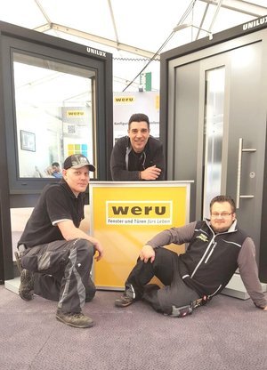 Drei Mitarbeiter präsentieren Weru Fenster und Türen an einem Messestand mit Weru-Logo.